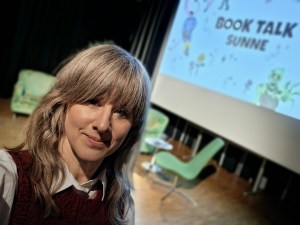 En kvinna i förgrunden, i bakgrunden en storbildsskärm med texten Book Talk Sunne.